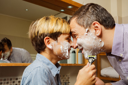 Dad with son shaving foam on face touching foreheads, laughingの写真素材