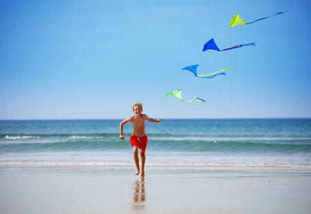 Boy run on the beach holding a colorful kite groupの写真素材