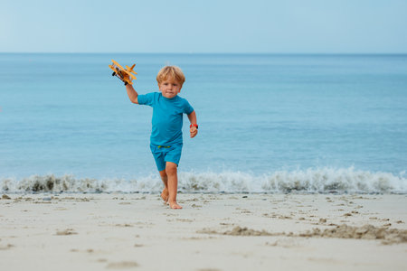 Blond boy run with boat toy model at the beachの写真素材