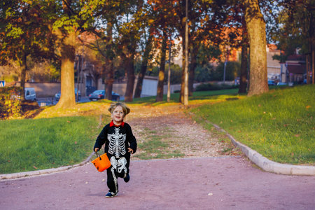 Boy run in skeleton disguise hold bucket for candies at park
