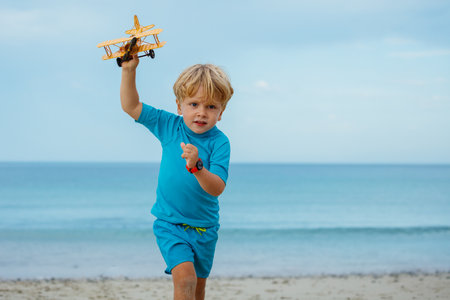 Portrait boy run with toy model of the plane hat over calm oceanの写真素材
