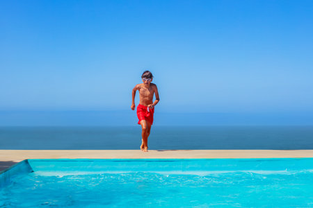 Happy boy jump into resort pool with sea line on backgroundの写真素材