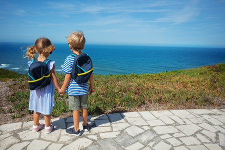 Boy and girl with backpacks admire sea from hill on summerの写真素材