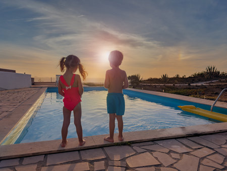 Kids, boy and girl stand by a pool at sunset, ready to swimの写真素材