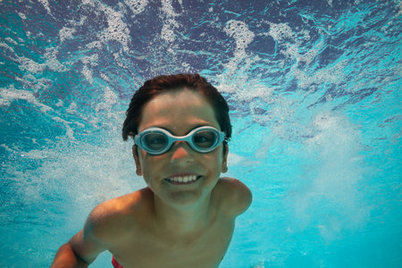 Child boy dives happily in clear pool water at summer resortの写真素材