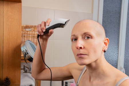 Hairless lady look at camera uses electric razor to shave headの写真素材