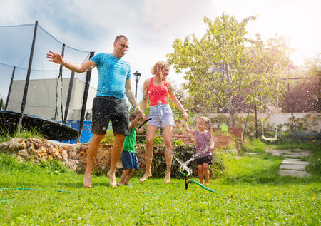 Joyful parents and kids engaged in water play outside houseの写真素材