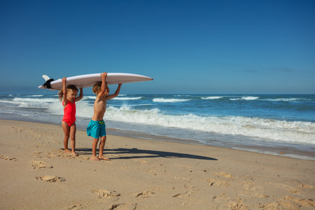 Kids walking with surfboard on shoulders at sunny ocean beachの写真素材