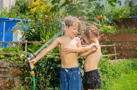Happy young boy and girl enjoy refreshing water game with hoseの写真素材