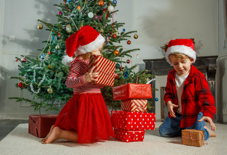 Kids in Santa hats open presents by a decorated Christmas treeの写真素材