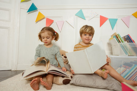 Two siblings reading books together in a cozy, colorful bedroomの写真素材
