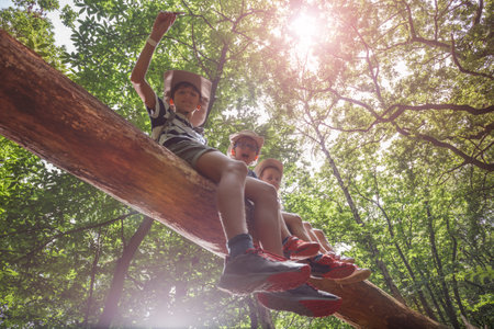 Three happy kids scouts brave sit on high log in sunlit forestの写真素材