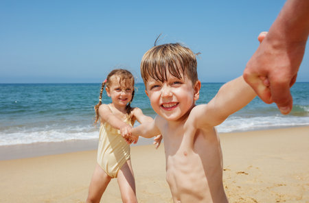 Smiling children playing by the ocean, holding hands happilyの写真素材