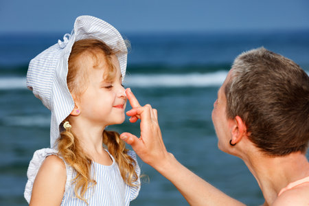 A little girl get sunscreen applied by an adult at the seasideの写真素材