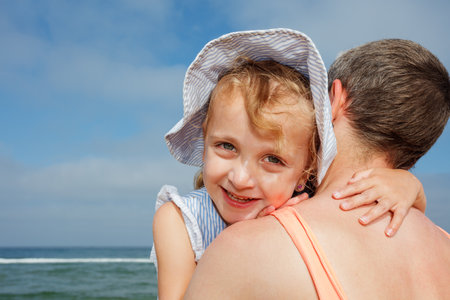 A happy child girl hugs her mother at the beach under blue skyの写真素材