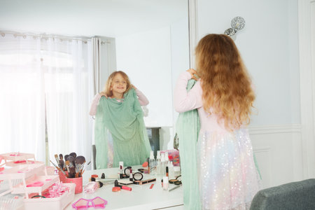 A happy child admires herself in mirror, holding up moms dressの写真素材