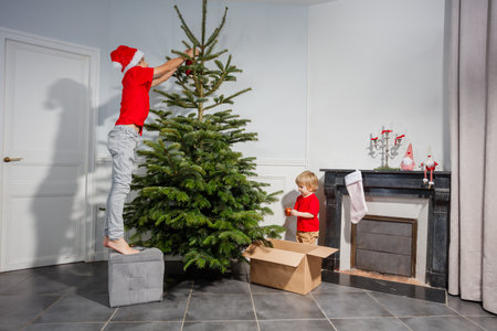Young boys in Santa hat start decorating Christmas tree togetherの写真素材