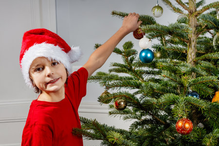 Young boy in red Santa hat reach out to decorate Christmas treeの写真素材