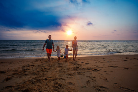 A family holds hands while walking on the beach at summer sunsetの写真素材