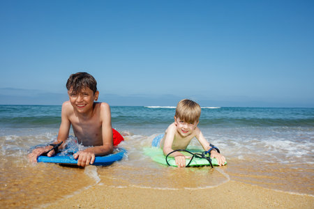 Kids catching waves, smile, and enjoy the beach on their boardsの写真素材