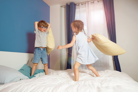 Siblings having fun with a pillow fight in their parents bedroomの写真素材