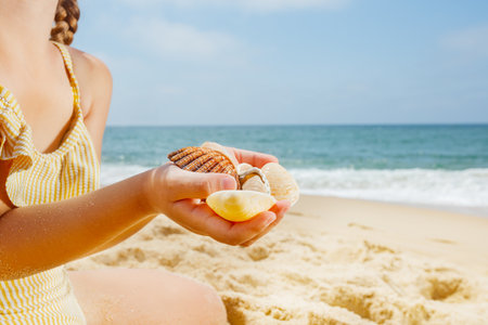 A handful of seashells in kid hands, the sunny beach background