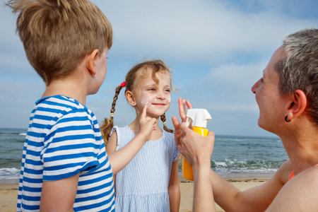 Happy mother with kids at beach applying sunscreen cream on faceの写真素材