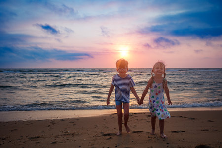 Two kids hold hands in hand stroll along the shore at sunsetの写真素材