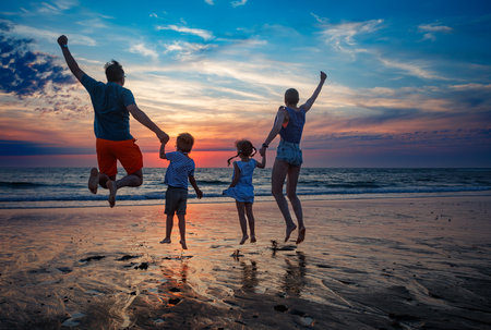 Family with kids joyfully jumps together on a beach at sunset