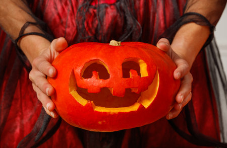 Closeup of woman hands holding joyfully carved Halloween pumpkinの写真素材