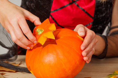 Woman in black and red costume carving a large orange pumpkinの写真素材