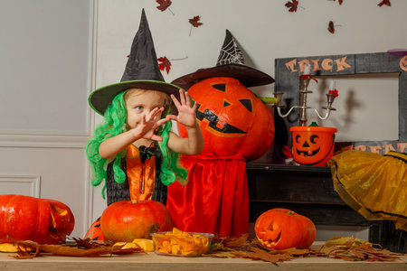 Cute child witch on Halloween make spooky gestures while carvingの写真素材