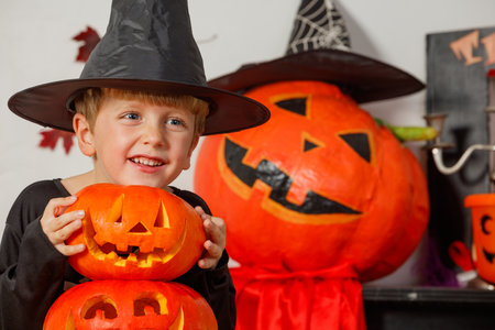 Boy in Halloween costume is behind a stack of carved pumpkinsの写真素材