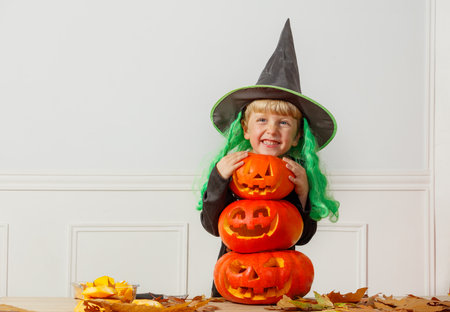 Kid have fun in witch hat and skeleton costume with pumpkinsの写真素材