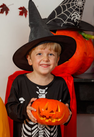 Happy kid boy in spooky wizard disguise holding carved pumpkinの写真素材