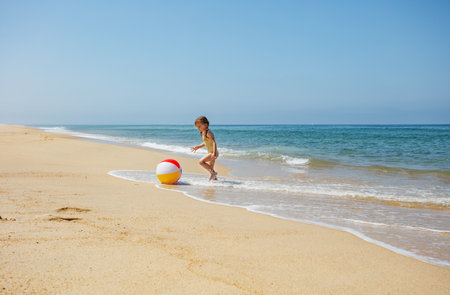 A child girl plays with beach ball on sandy, sunny shorelineの写真素材