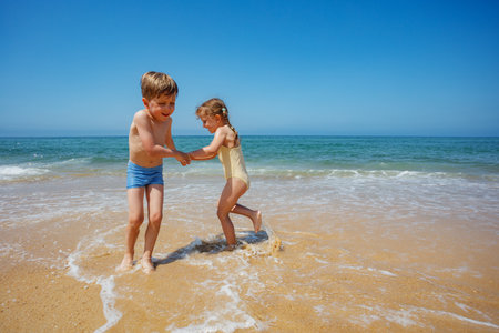 Children enjoy sunny day by the seaside dancing turning aroundの写真素材
