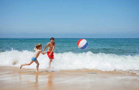 Two boys are splashing in waves playing beach ball on vacationsの写真素材