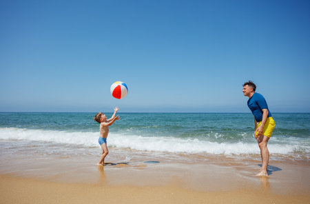 Joyful beach day father and son enjoy playing with ball togetherの写真素材