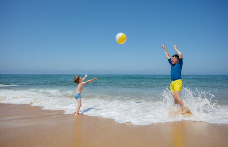 Sun, sea, smiles as dad and little kid have fun with beach ballの写真素材