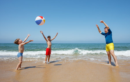 Man and young boys playfully pass beachball along the oceanfrontの写真素材