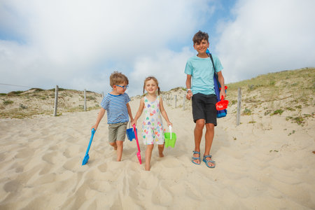 Smiling children holding buckets on a sandy path to the beachの写真素材