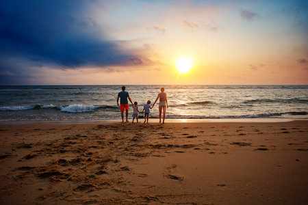 A group of four family members stroll on sandy shore at sunsetの写真素材