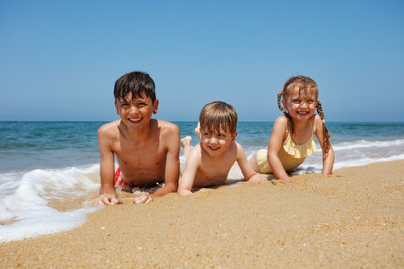 Smiling children lay at the beach, having fun in sun and sandの写真素材
