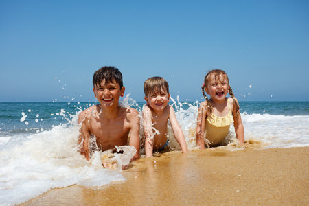 Happy kids playing on beach by the ocean waves at a sunny dayの写真素材