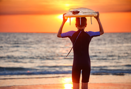 Surfer admiring stunning ocean sunset while holding his boardの写真素材