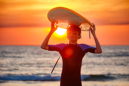 Teen with a surfboard overhead, enjoys beach walk during sundownの写真素材