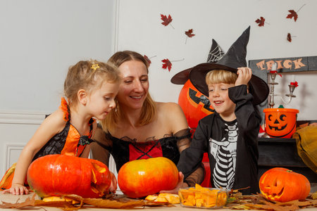 Kids and mother laughing carving pumpkins in festive costumesの写真素材