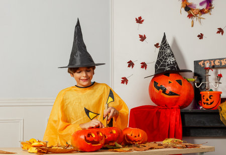 Child in a witch costume carving Halloween pumpkins with joyの写真素材