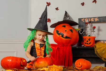 Girl in Halloween costume carving pumpkins prepare decorationsの写真素材